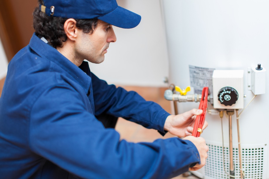 Plumber wearing a hat fixing a residential water heater with a wrench