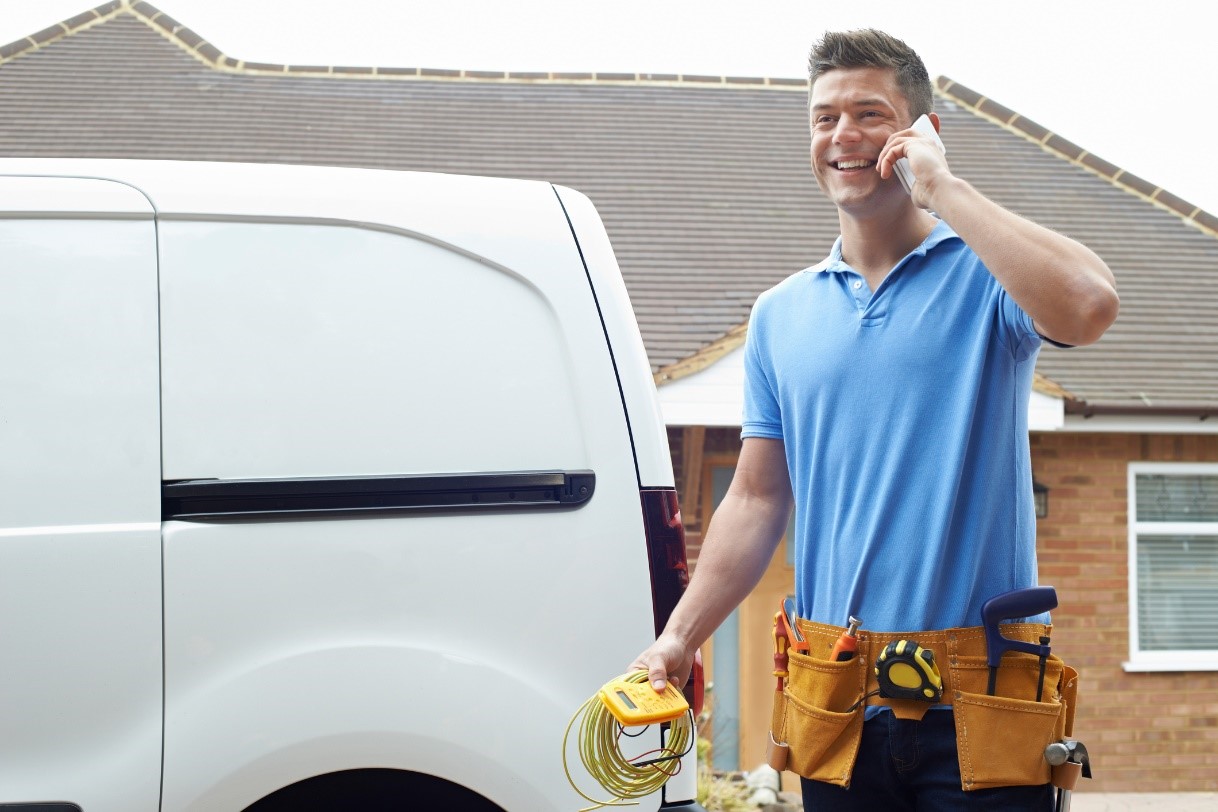 Technician on the phone standing in front of their white work van